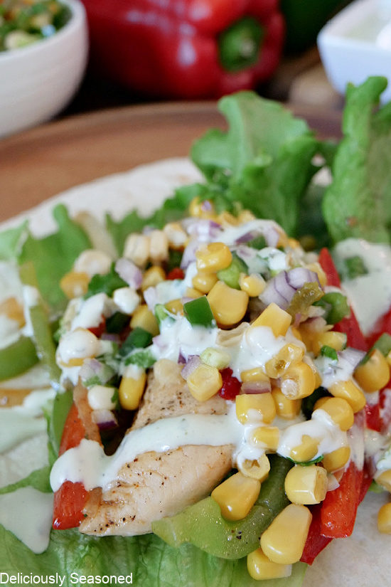 A flour tortilla with lettuce, chicken, peppers, corn salsa and avocado ranch dressing on it.