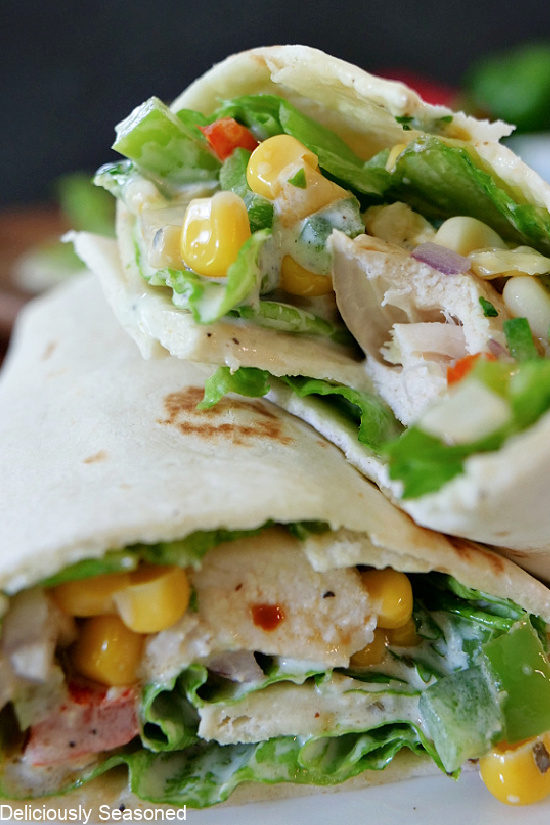 A close up photo of a Southwest Chicken Wrap but in half with a bite taken out of one of the halves, showing all the ingredients inside the wrap.
