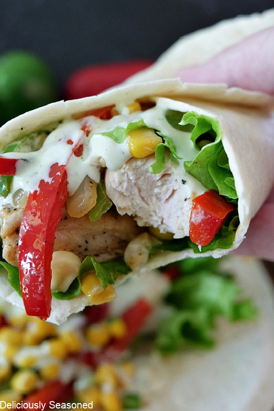 A close up photo of a Southwest Chicken Wrap being held up with a bite taken out of it showing all the ingredients inside.