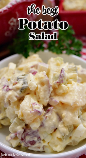 A close up photo of a white bowl filled with a serving of potato salad.