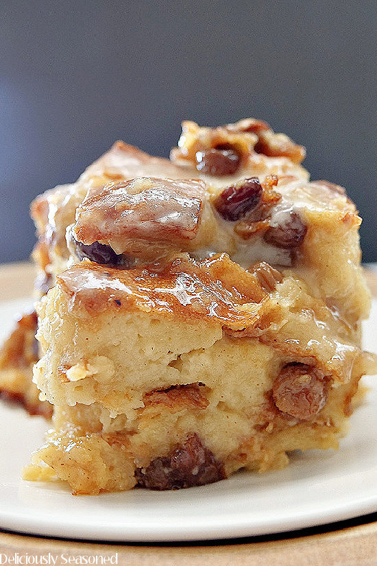 A slice Cinnamon Raisin Bread Pudding on a white plate, full of raisins, cinnamon, and topped with a glaze.