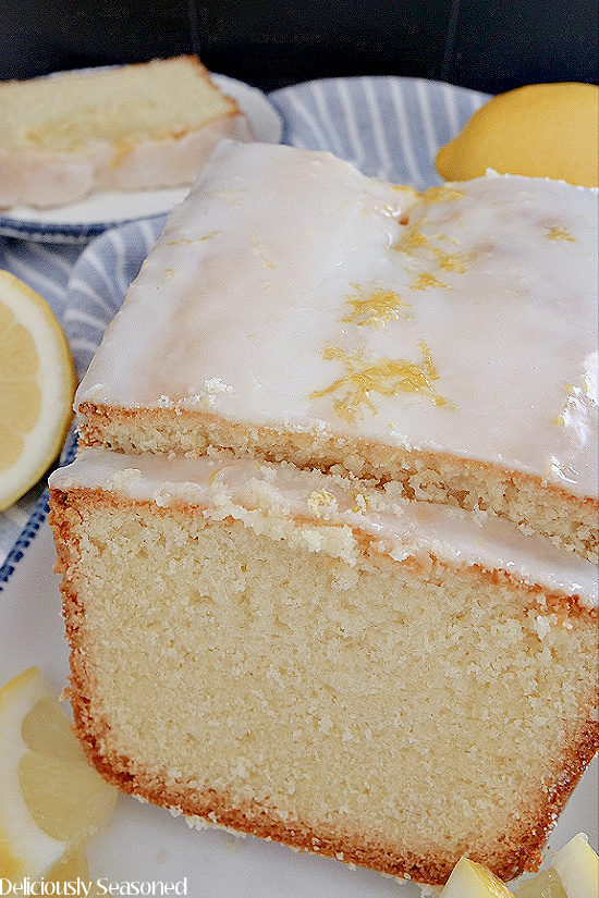 A close up view of a lemon pound cake with a slice cut both on a white plate with blue trim.