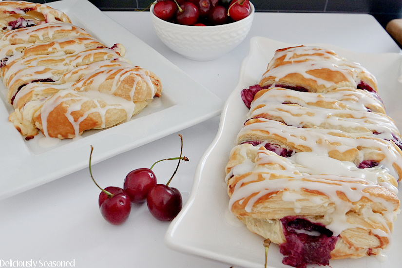 Two Cherry Cream Cheese Danish puff pastries white plates before being sliced and served.