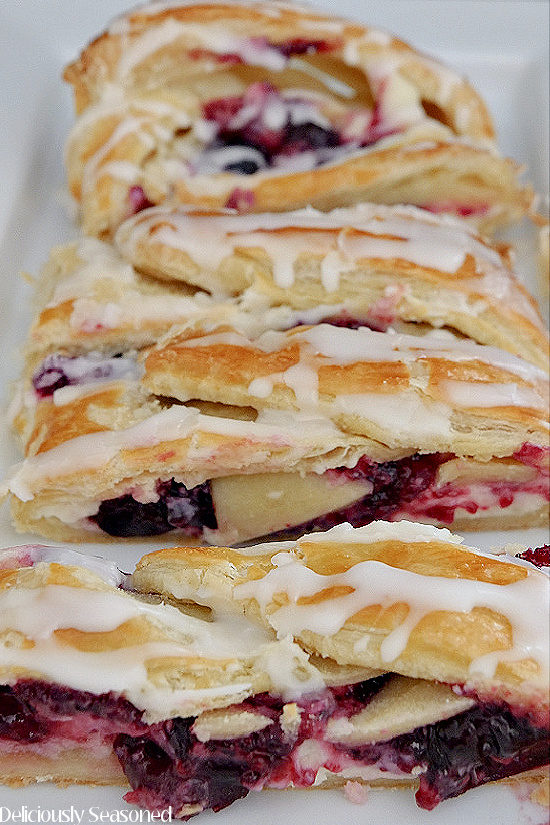 A Cherry Cream Cheese Danish on a white plate that has been sliced showing the flaky layers and inside filling.