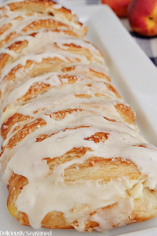 A peach cream cheese danish on a white plate before being sliced into serving pieces.