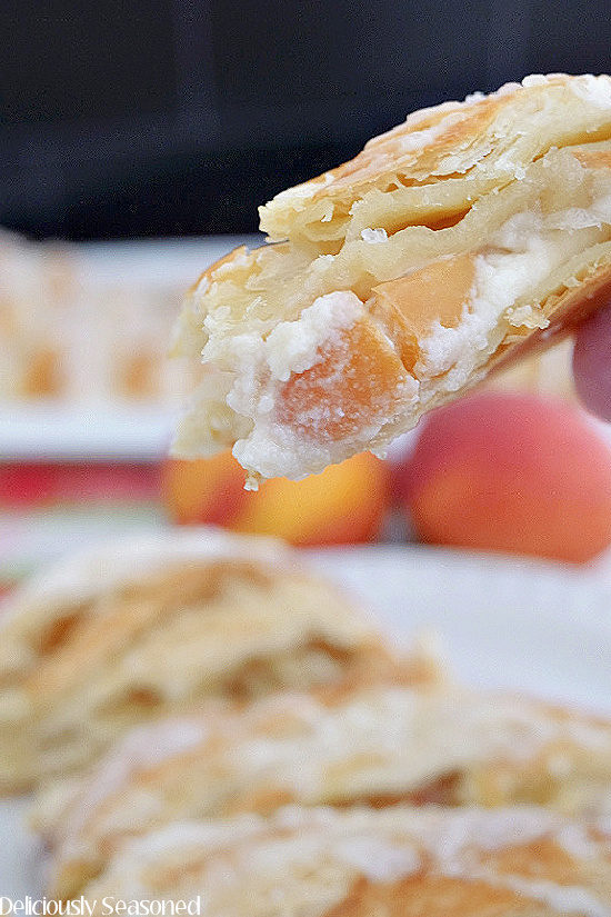 A slice of peach cream cheese danish being held up close to the camera lens to show the filling inside.