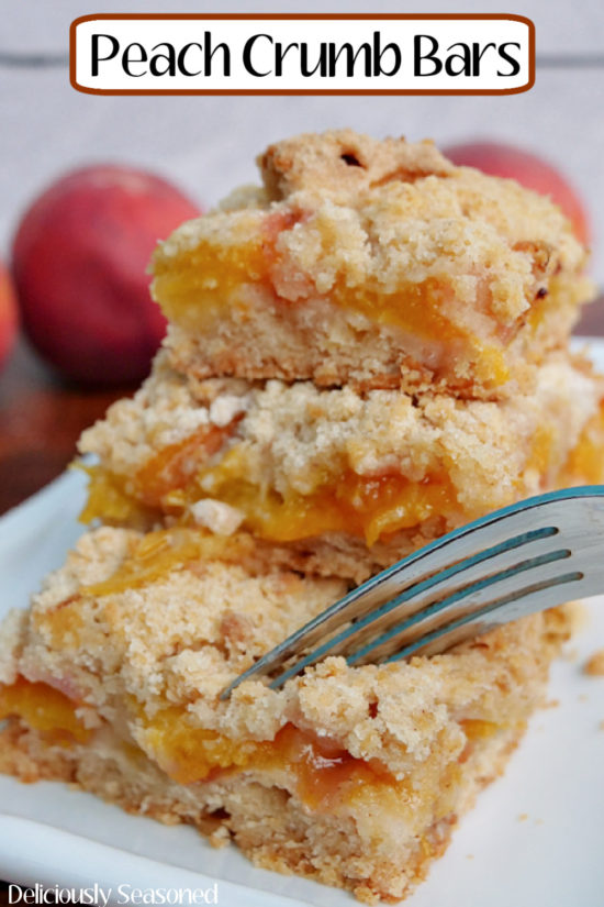 Three peach crumb bars stacked on top of each other with a fork getting ready to get a bite of the dessert.