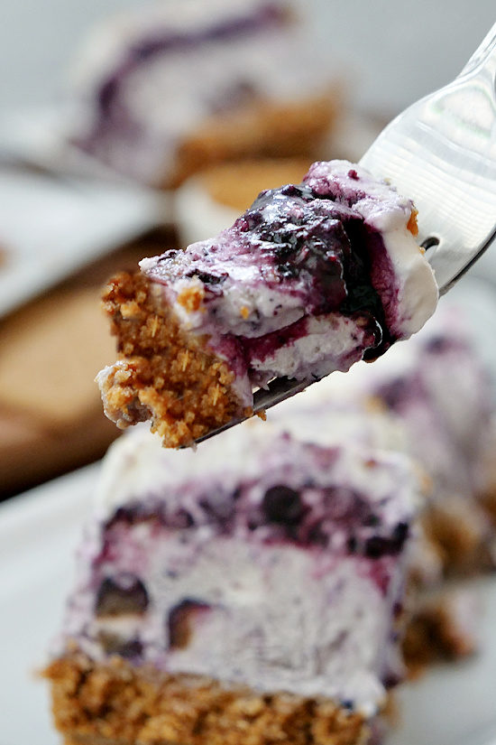 A fork holding a bite of frozen blueberry dessert above the plate with the remaining dessert on it.