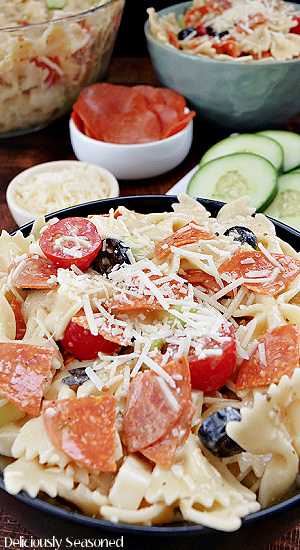 A close up shot of a black bowl filled with bow tie pasta salad.