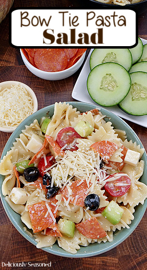 A greenish blue bowl filled with bow tie pasta salad with the title of the recipe at the top in the center.