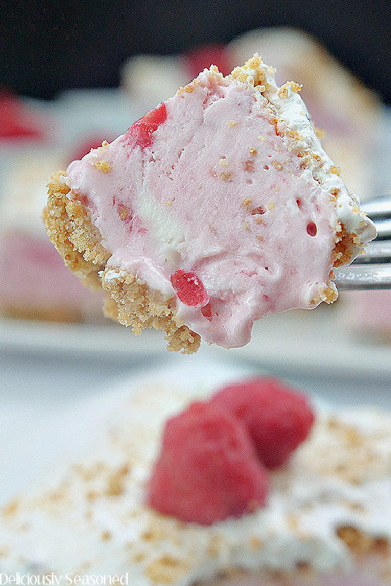 A close up shot of a bite of frozen raspberry dessert on a fork being held above a slice of the dessert.