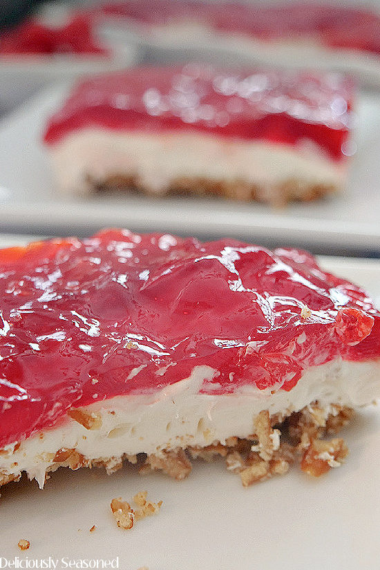 A close up photo of a piece of raspberry pretzel salad on a white plate with another piece in the background.