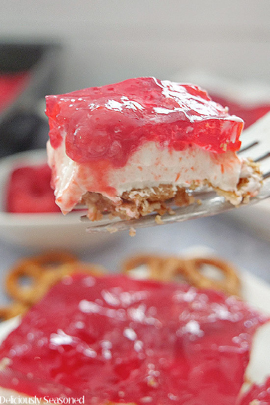 A forkful of raspberry pretzel salad being held up close to the camera lens showing the three layers.