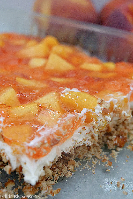 Layered peach pretzel salad layered in a glass dish with a pretzel crust, a whipped filling, and a peach jello topping.