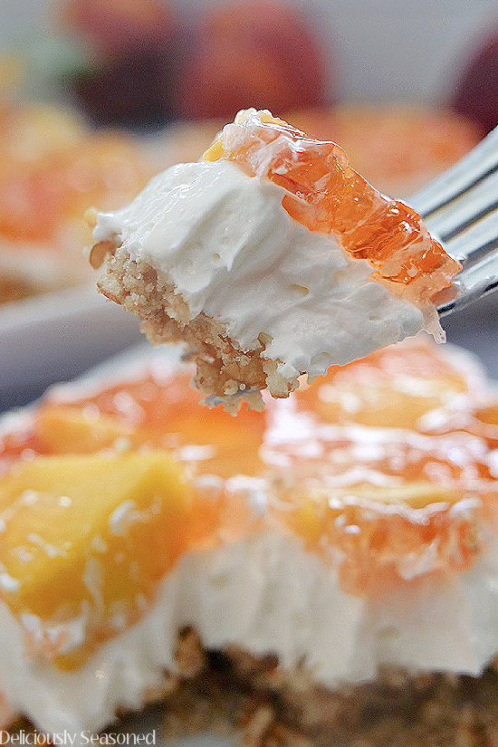 A bite of peach pretzel salad on a fork, with a piece of dessert sits in the background.