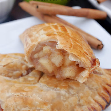 Two apple hand pies on a white plate with cinnamon sticks and an apple in the background.
