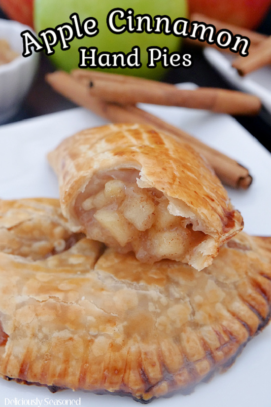 Two apple hand pies on a white plate with cinnamon sticks and an apple in the background.
