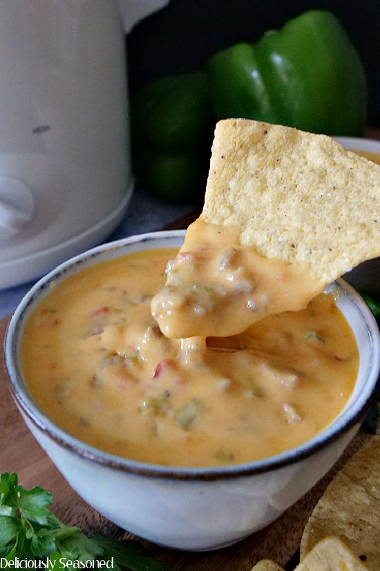A grey bowl filled with crock pot queso with Italian sausage and a tortilla chip held up with the dip showing on the chip.