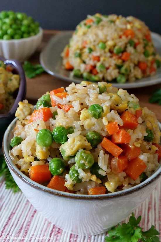 A small white bowl of fried rice with carrots, peas, and egg.