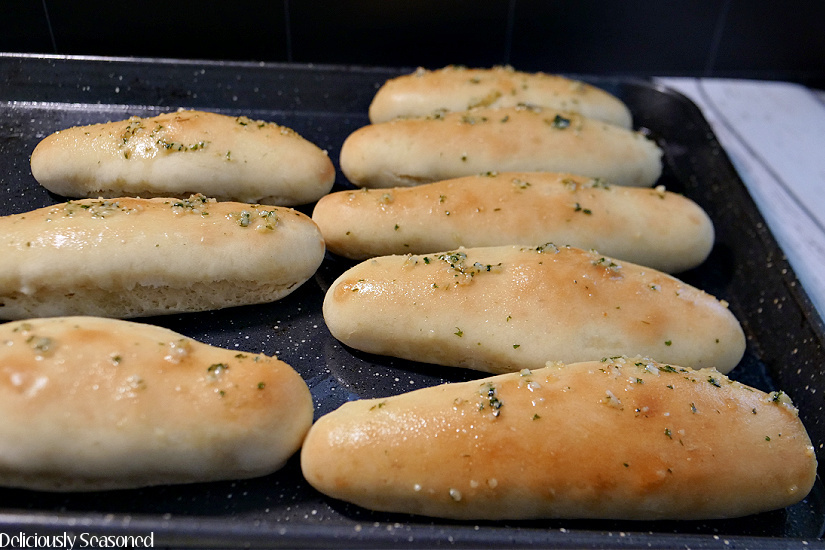 A dark colored baking sheet with 8 breadsticks on it after being pulled from the oven.