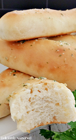 A close up of four breadsticks with one with a bite taken out.