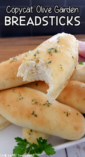 A close up photo of a breadstick half eaten being held above a white plate with more breadsticks on it.