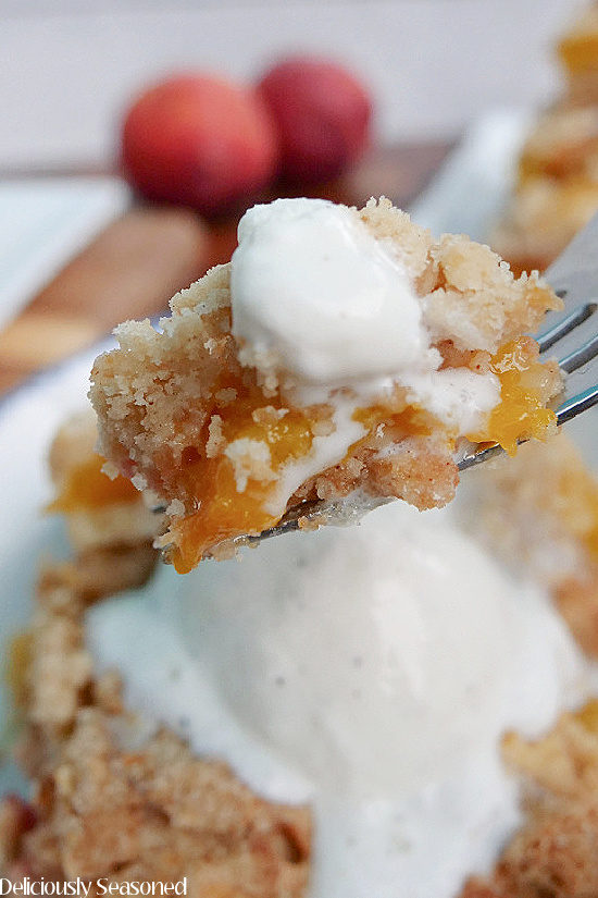 A super close up of a bite of peach crumb bar with a little vanilla ice cream on a fork.