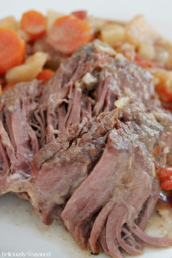 A close up photo of a piece of crock pot chuck roast with potatoes and carrots in the background.
