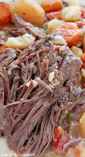 A super close up of a slice of chuck roast with potatoes and carrots in the background.