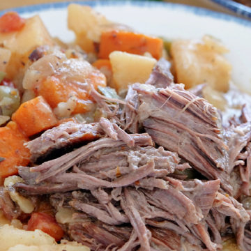 A white plate with tender chuck roast and vegetables on it.
