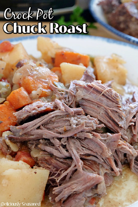 A white plate with blue trim with crock pot chuck roast on it along with potatoes and carrots.