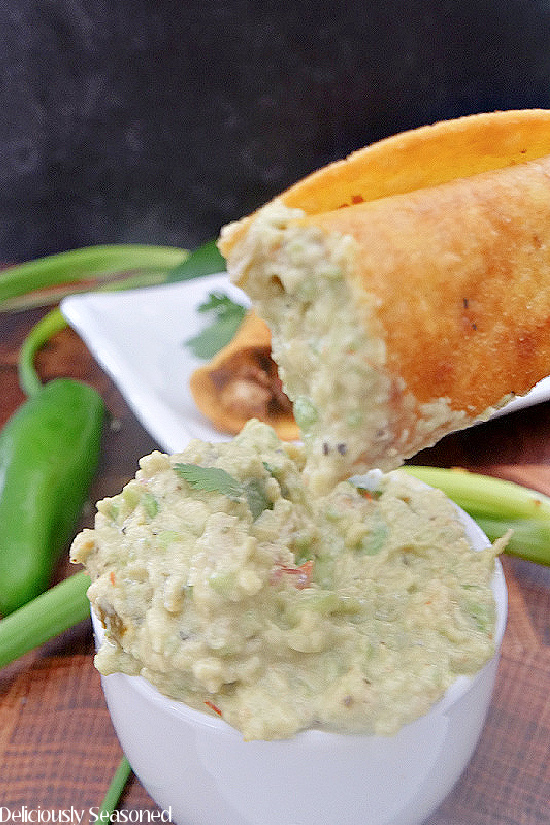 A chicken taquito with a bite taken out being held above guacamole after being dipped into it.