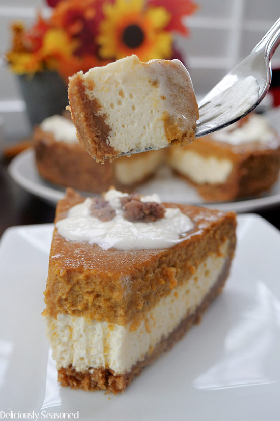 A slice of pumpkin cheesecake on a white plate with a bite of cheesecake on a fork held above the slice.