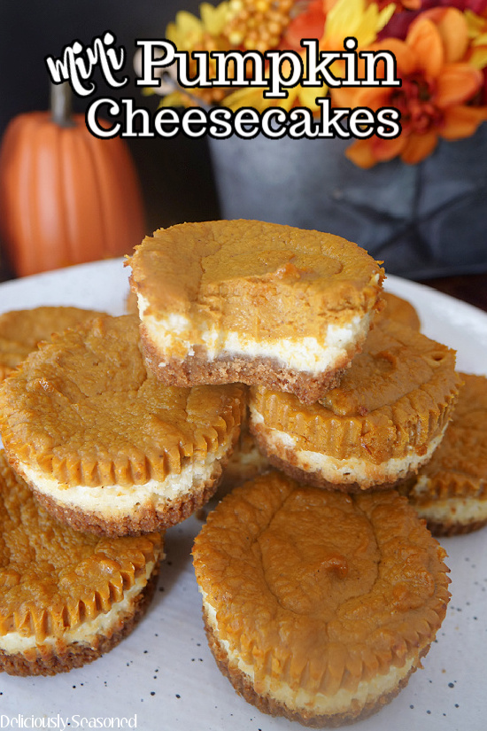 Mini Pumpkin Cheesecakes stacked up on a white plate, with a bite taken out of one.
