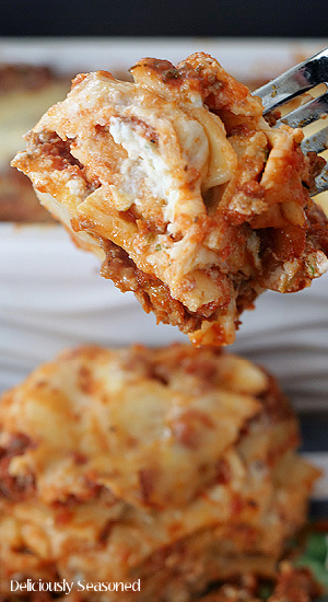 A bite of lasagna on a fork held close to the camera for a close up shot.