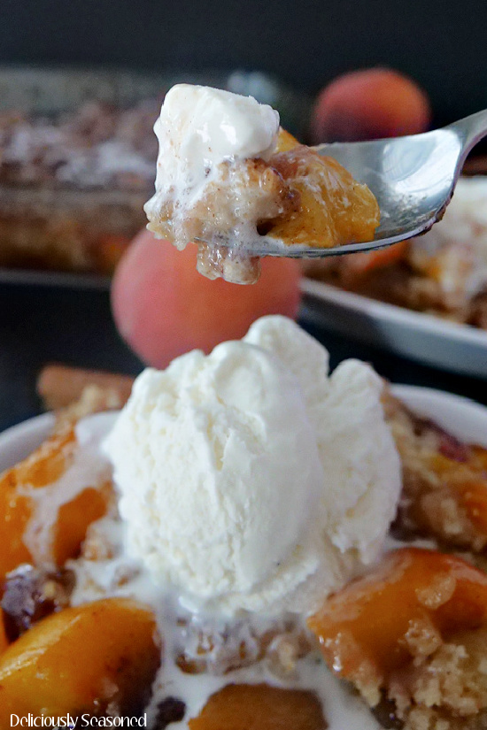 A white dish filled with peach cobbler and topped with a big scoop of vanilla ice cream.