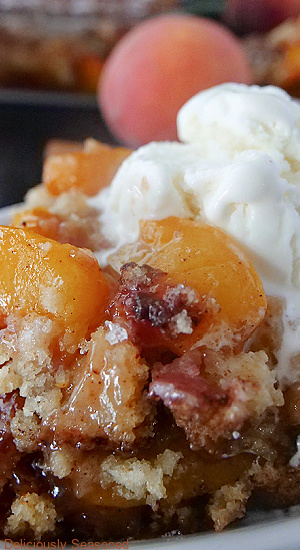A close up photo of a bowl of peach cobbler with a scoop of vanilla ice cream on it.