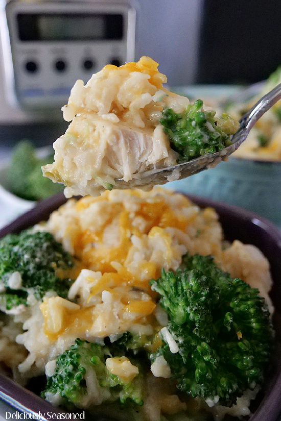 A super close up photo of a spoon filled with a bite of chicken broccoli and rice held above a bowl filled with the same.