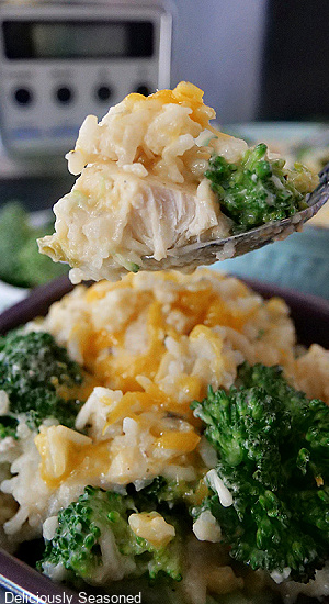 A close up shot of a spoon with chicken broccoli and rice on it.