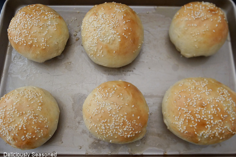 A horizontal photo of a baking sheet that is lined with baked hamburger buns.