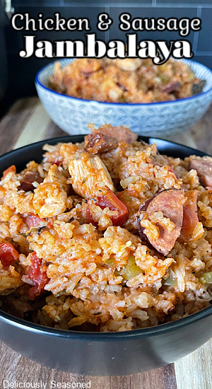 A black bowl with a serving of chicken and sausage jambalaya with a blue and white bowl in the background.