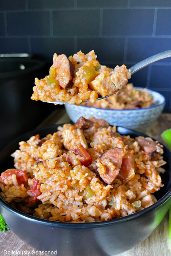 A black bowl full of jambalaya with a large spoonful overhead.
