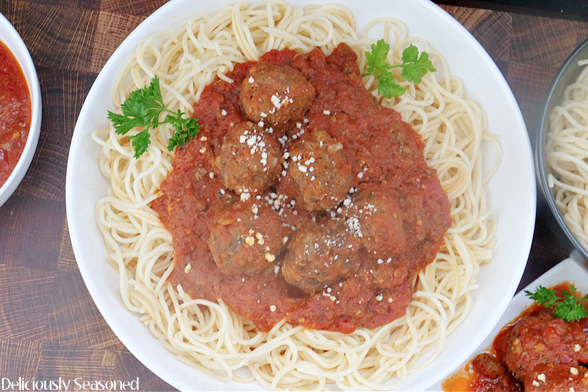 A large white bowl filled with spaghetti noodles and topped with a homemade meat sauce and meatballs.