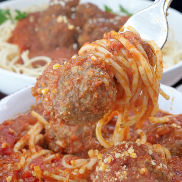 A white bowl with spaghetti noodles, meat sauce, and meatballs, with a large bite on a fork with a whole meatball on it.
