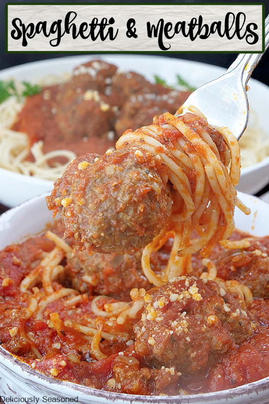A white bowl with spaghetti noodles, meat sauce, and meatballs, with a large bite on a fork with a whole meatball on it. 
