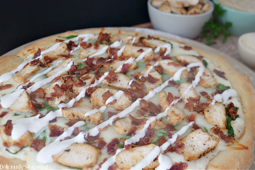 A picture of an uncut chicken bacon ranch pizza on a pizza pan.