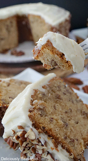 Two slices of butter pecan pound cake on a white plate with white frosting on it and chopped pecans with a bite sitting on a fork.
