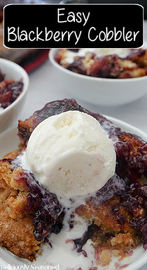 A close up of a white bowl filled with homemade blackberry cobbler with a scoop of vanilla ice cream on top.