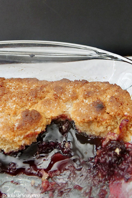 A close up photo of blackberry cobbler in a glass baking dish showing the cobbler topping and filling.