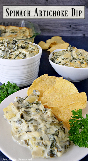 A white plate and two white bowls with spinach artichoke dip in them with tortilla chips placed on the plate.